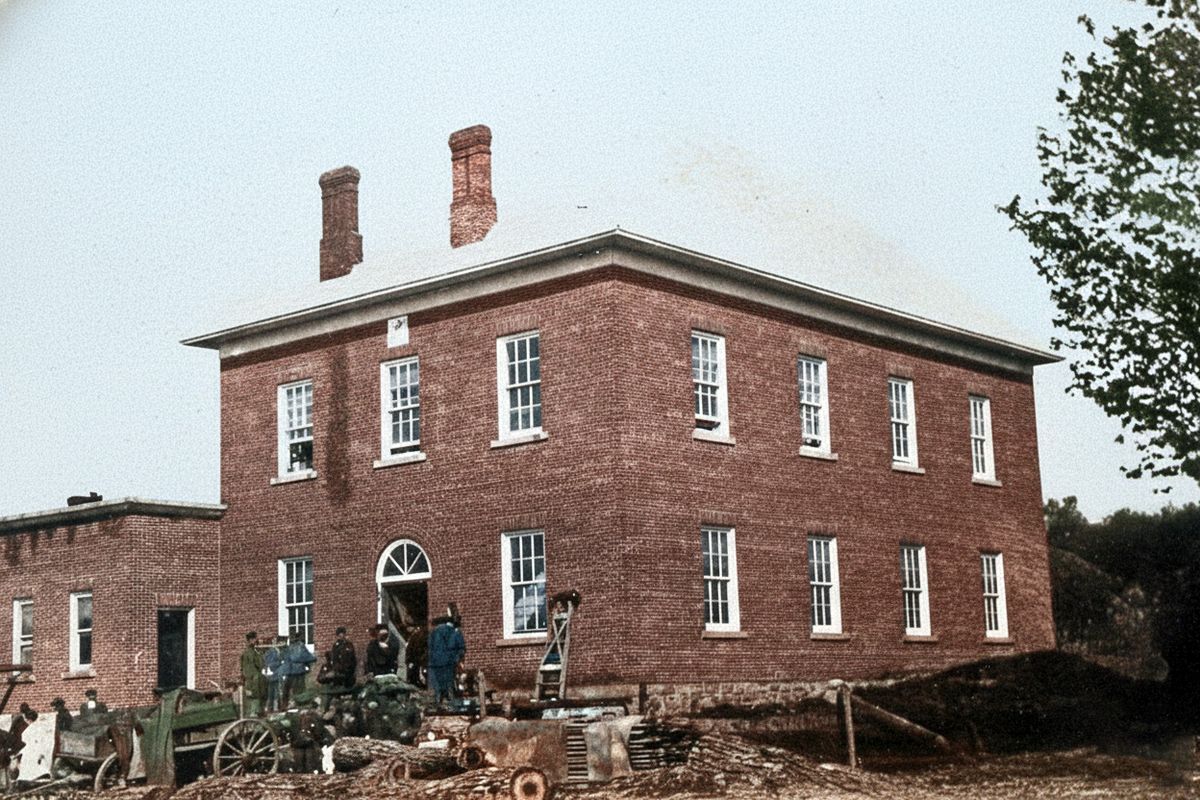 Old Town Hall c.1900\n\nThe date is unclear, the left side addition doesn't appear on the 1897 insurance map of Delta, it was a later addition.  The tree on the right appears to be a similar size to a photo dated to the early 1900s.\n\nThe stain on the left side, present to this day, is creosote, likely from liquid creosote wicking through unlined, porous brickwork due to a combination of burning wet wood and a deteriorating internal mortar lining of the chimney.\n\nThe logs in the front are destined for the sawmill that was attached to the Old Stone Mill.\n\nThe reason for the men, several in uniform, is unclear.