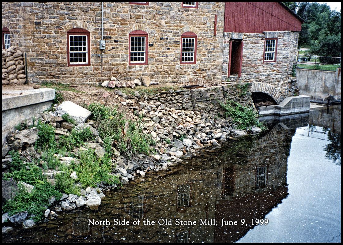 North Side and Buffer Wall\nA unique feature to the Old Stone Mill was the buffer wall, originally built in 1810-11. \n Since the mill acted as it's own dam (stoplog dam at the head of the mill's bywash), the wall was vulnerable to things such a ice and spring flooding debris.\n The solution was to build a wall that extended out 7 feet, with openings into the millraces.  \nThe top of the waterwheel headrace is just barely visible. \n\nIn c.1861, with the building of the turbine hall (right side) the buffer wall was extended to also protect the turbine headrace.\n\n  It was removed by MNR after they built a new dam upstream of the mill in1962 to expose the turbine raceway and\n to allow for stabilization of the bywash, which including the cement wall that can be seen in this photo.